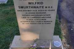 Close-up sandstone memorial plaque — Wilfrid Smurthwaite M.B.E., beloved husband, father and grandfather